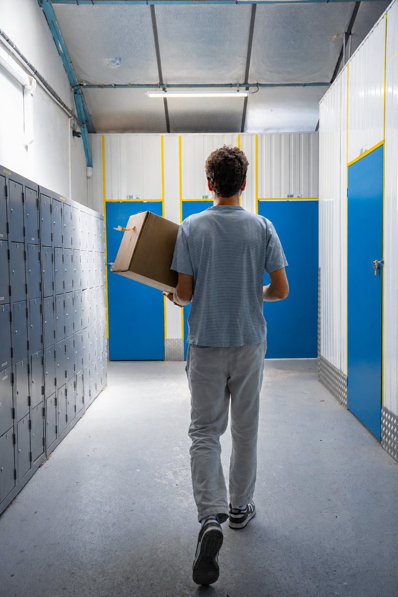 Un client porte un carton devant des box aux portes bleues
