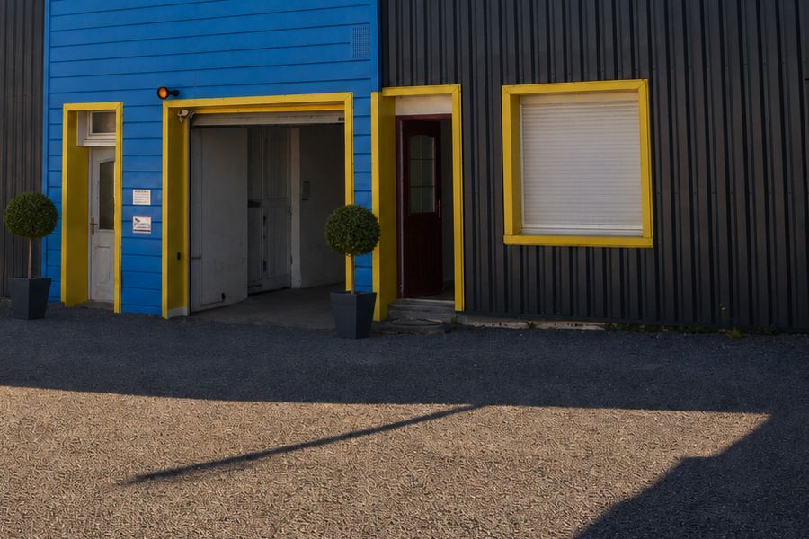 La cour gravillonnée devant le bâtiment du centre, portes à encadrements jaunes, en fin de journée